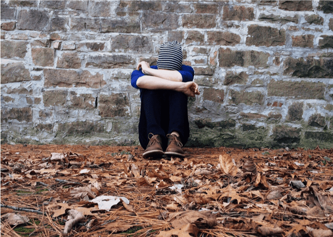 girl sitting outside against a wall crying into her arms