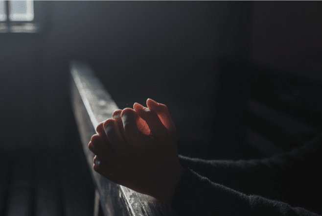 praying hands in a dark room with light from the window